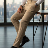 Man in a white shirt and beige pants sitting in an office with a cityscape view.